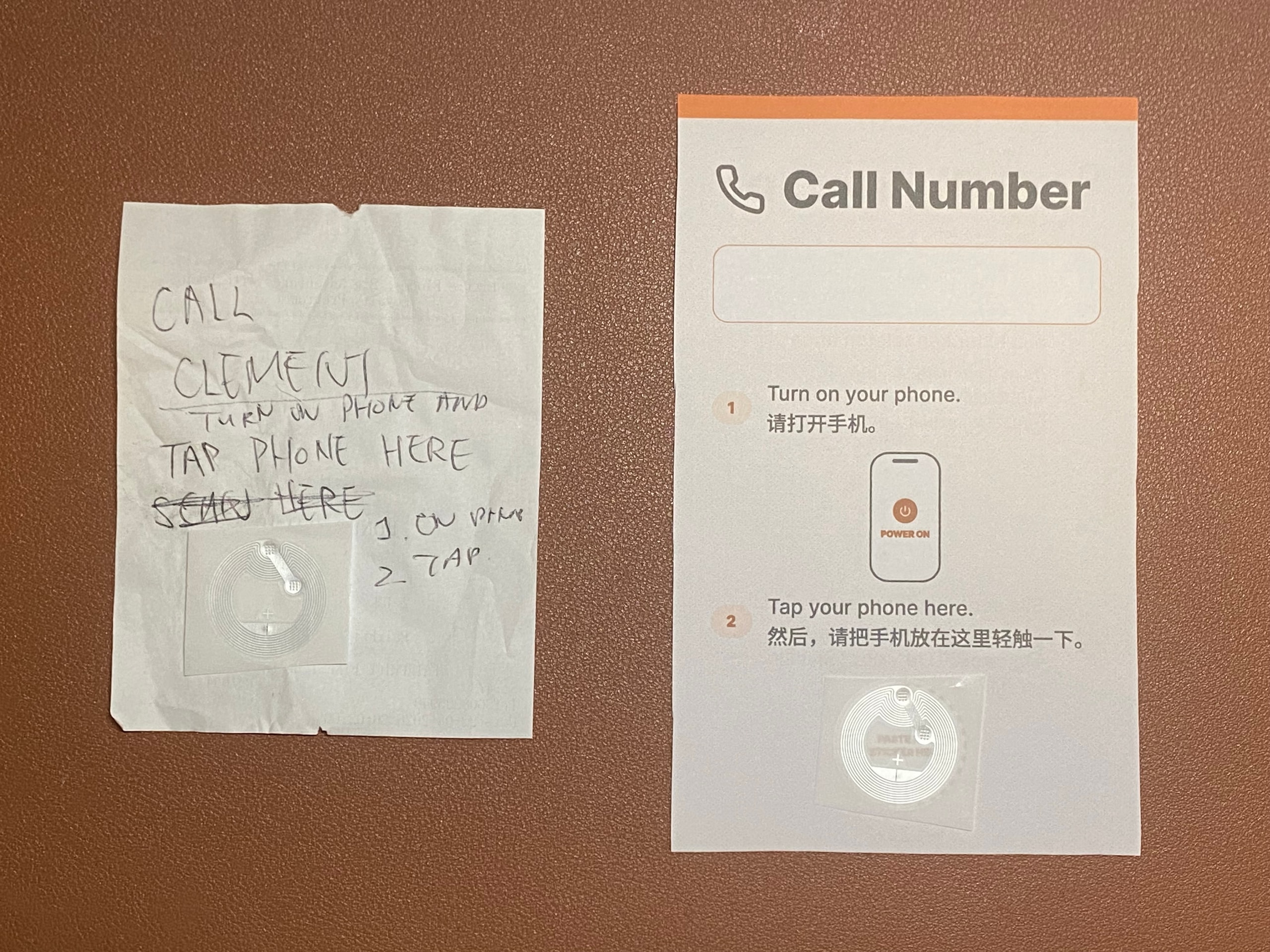 Two NFC prototypes side by side on a brown surface. Left: a crumpled scrap of paper with handwritten ‘Call Clement — turn on phone and tap phone here’, a crossed-out ‘Send here’, margin notes ‘1. On phone, 2. Tap’ and an NFC sticker. Right: a printed Call Number card with an orange top bar, a name field, two numbered steps in English and Chinese, a phone illustration and the NFC sticker.